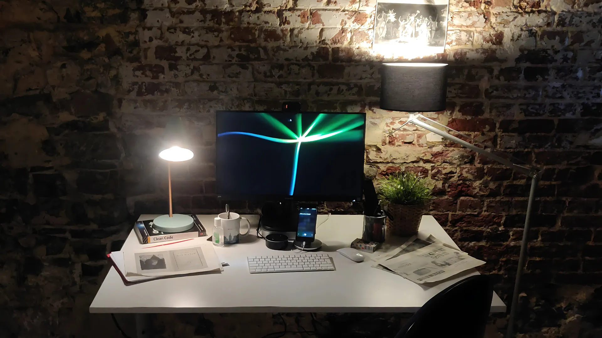 An image of a desk, with a screen, keyboard, and office ephemera, with a smartphone and Amazon Echo on it.
